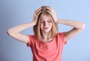 Cute girl suffering from headache on color background