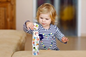 Adorable toddler girl playing with educational toys in nursery. Happy healthy child having fun with colorful different plastic blocks at home. Cute baby learning creating and building
