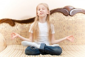 portrait of beautiful school young girl with long blond hair having fun sitting on sofa meditating winking & looking at camera with white copy space on the background image