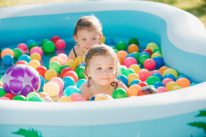The two little baby girls playing with toys in inflatable pool in the summer sunny day