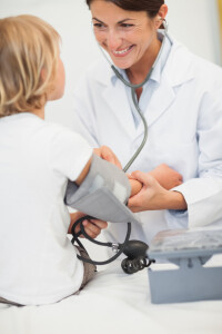 Smiling doctor measuring blood pressure of a child in examination room